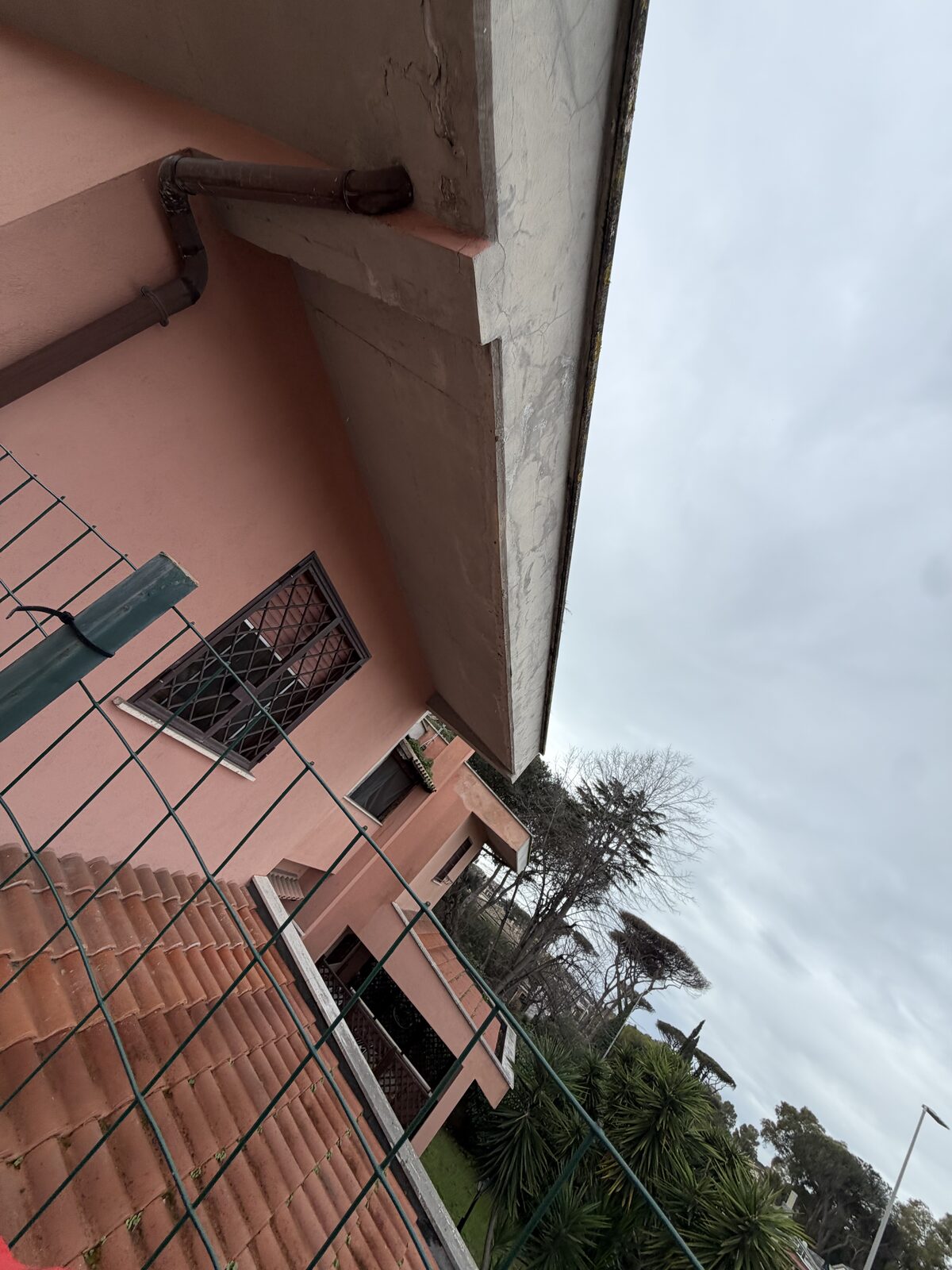 Cornicione di villa rosa con pluviale incassato e tegole sottostanti