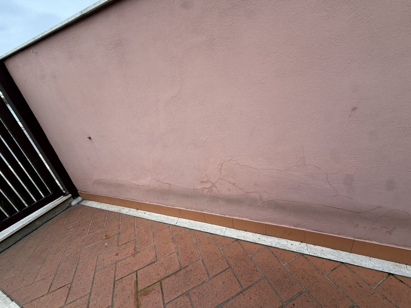 Muro perimetrale rosa con crepe diffuse e aloni di umidità alla base