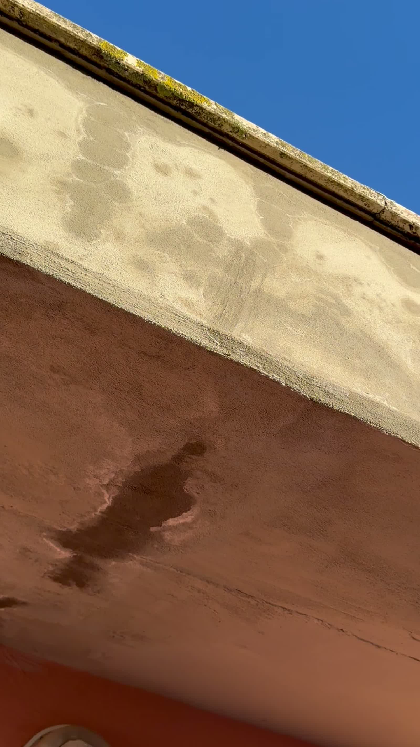 Facciata color terracotta con bolle e macchie da umidità sotto il cornicione